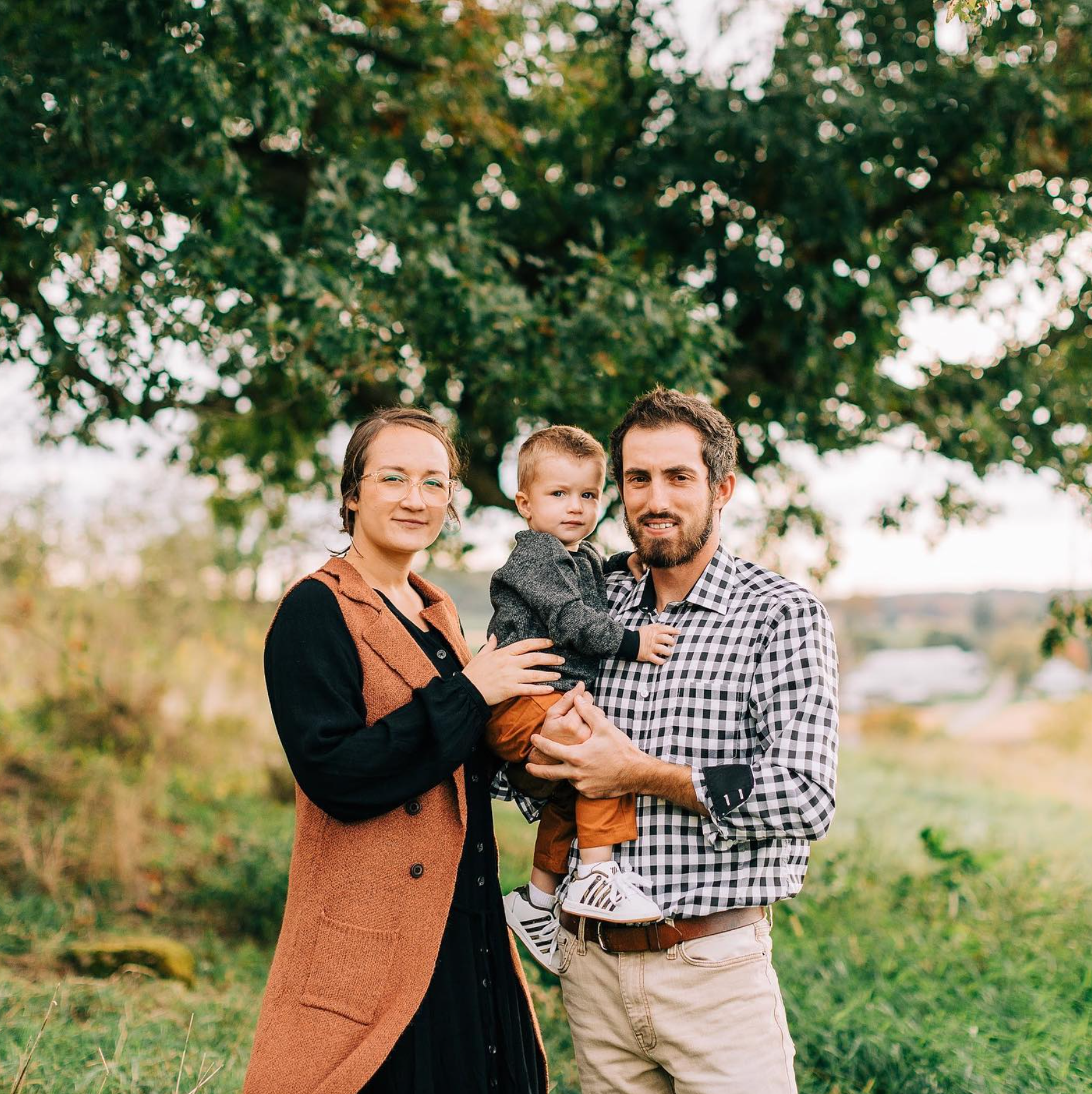Father and mother holding their baby in a family photo with an outdoor setting with
