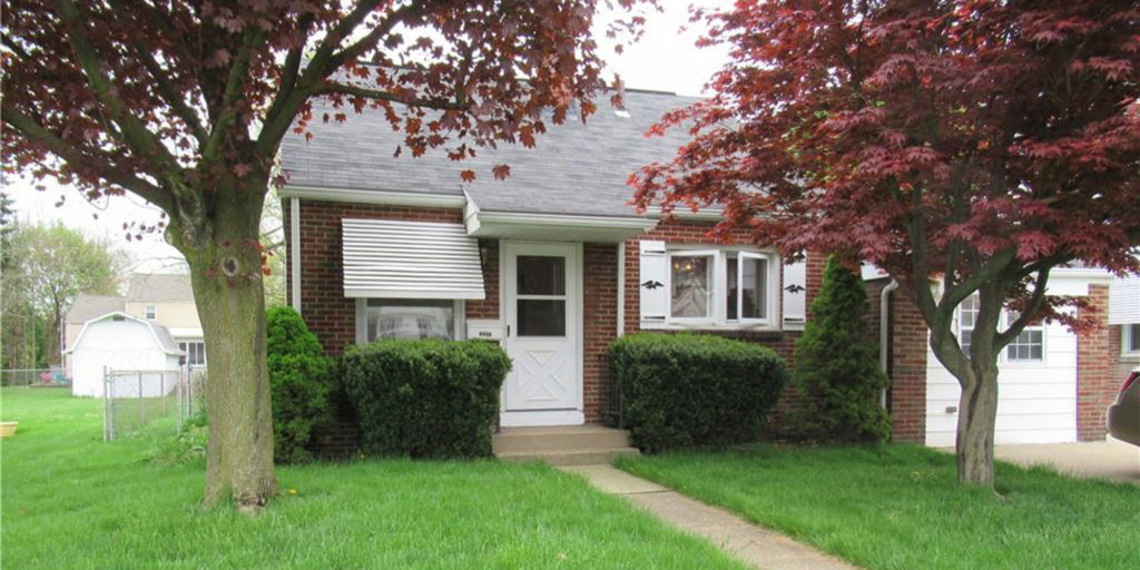 Red brick, one car garage home with trees in the front yard.